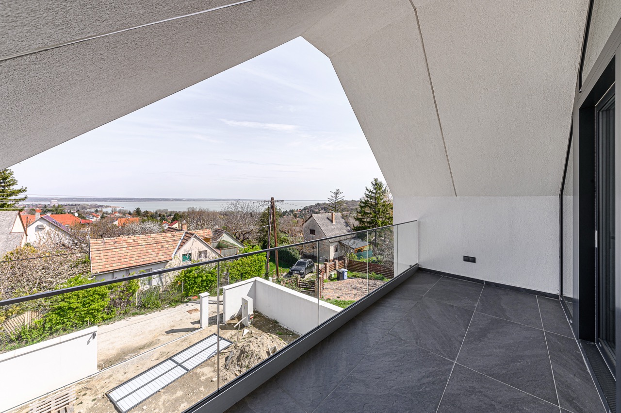 Modern terasz sötét járólappal és üvegkorláttal, panorámás kilátással a tóra